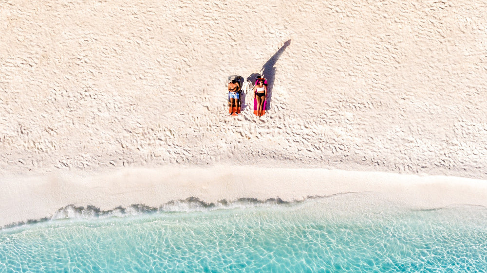 An aerial view of two beachgoers on empty white sand
