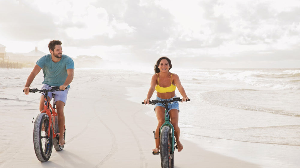 Two riders on electric bikes along the shoreline