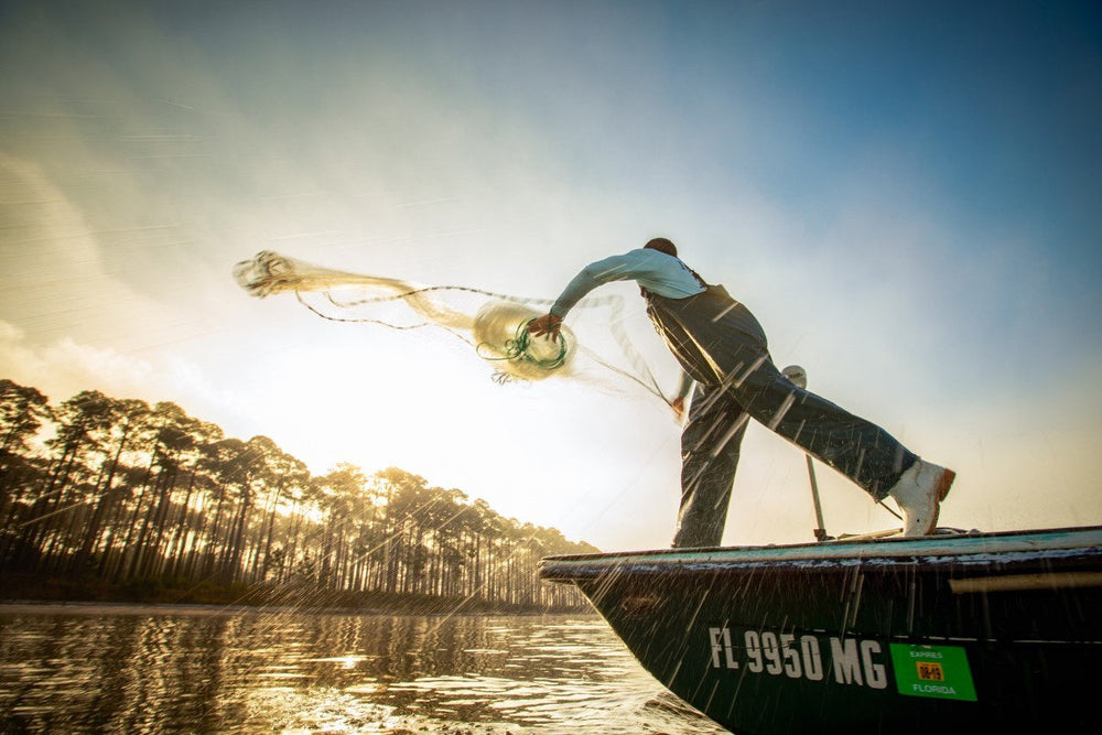 Fisherman throwing a cast net from a skiff at sunrise