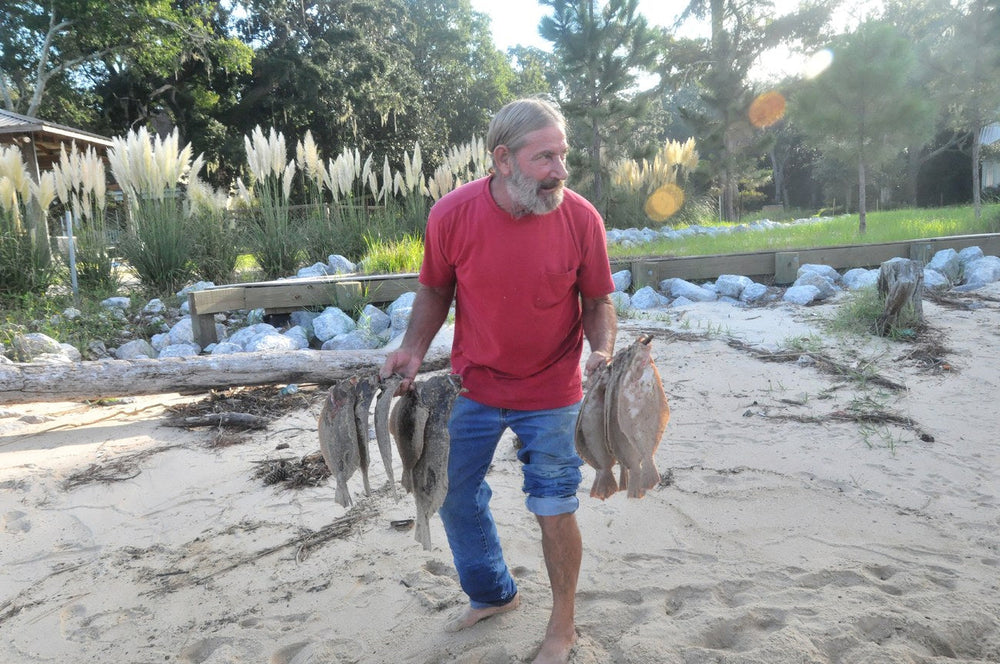 Man carrying a gigging pole strung with flounder up the beach