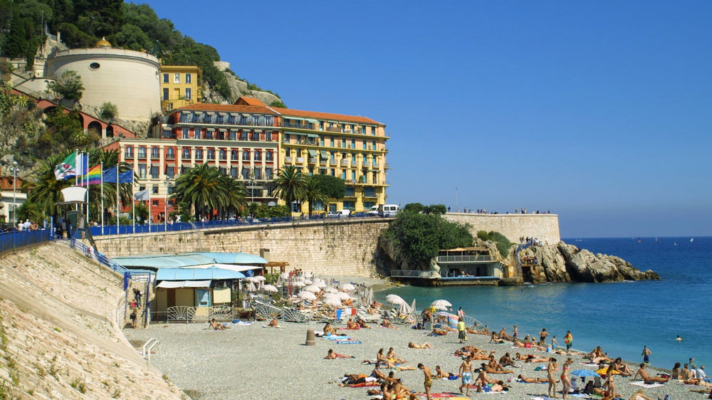 Sunbathers on the pebbled shoreline of Nice beneath the old town wall