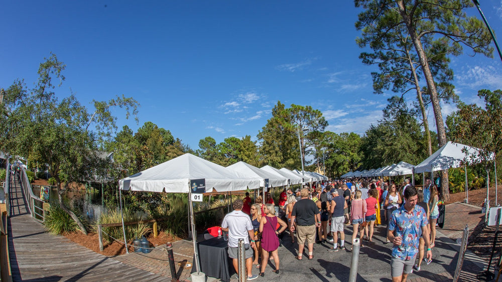 Crowds walking a boardwalk lined with white festival tents at a beer festival