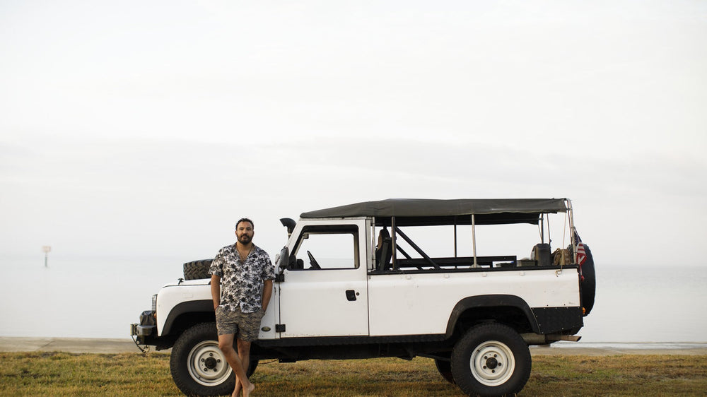 Daisson Hickel beside his white Land Rover Defender on a bluff above the water