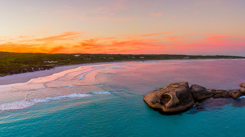 An aerial view at sunset of the pink-lit coastline and granite boulders at Esperance