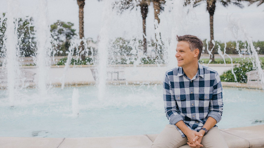 Sean Couch seated on the edge of a fountain beneath palm trees