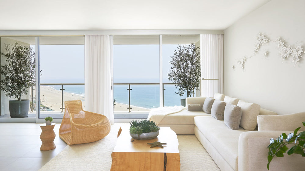 A pale, sunlit living room opening onto a Pacific ocean view