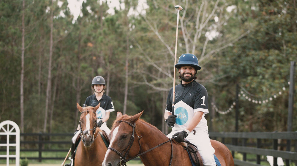 Two polo players on horseback beside the white barn at a Walton County ranch