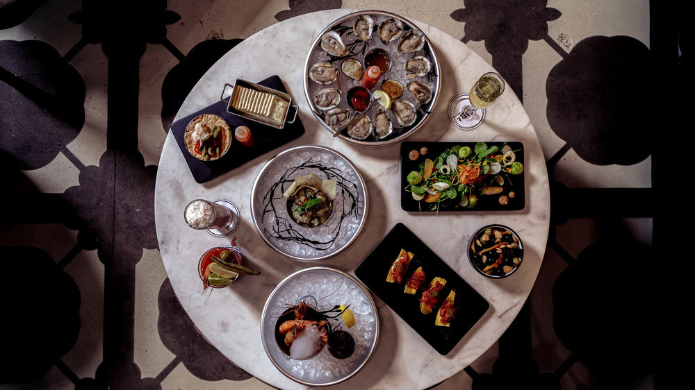 An overhead spread of oysters, small plates, and cocktails on a patterned table