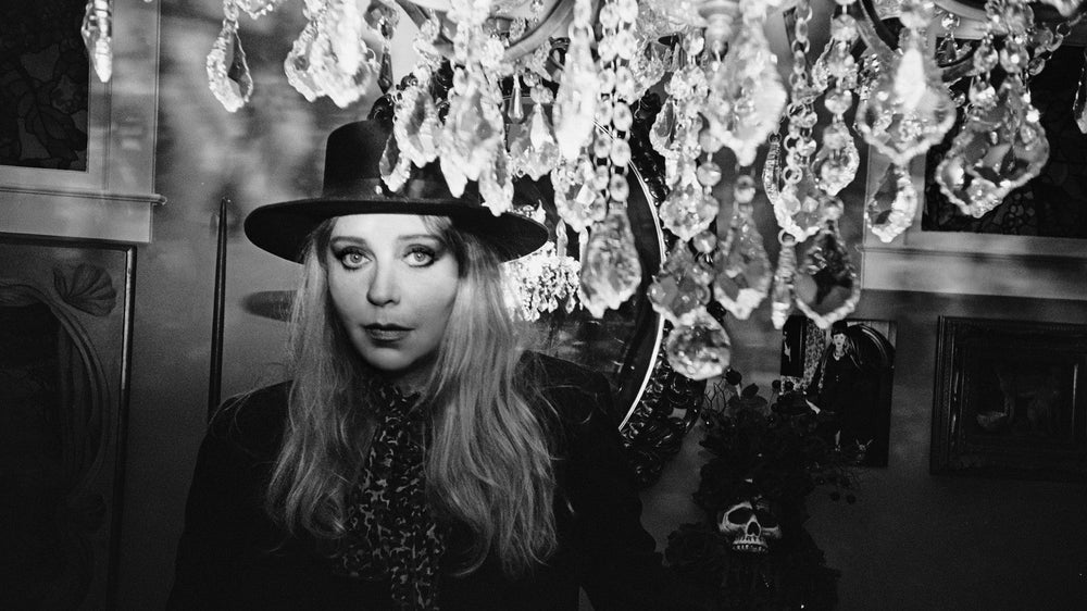 A black-and-white portrait of Bebe Buell in a wide-brimmed hat