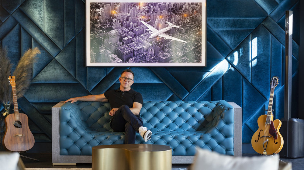 Dave King seated on a blue tufted sofa beneath a large artwork inside SOWAL House