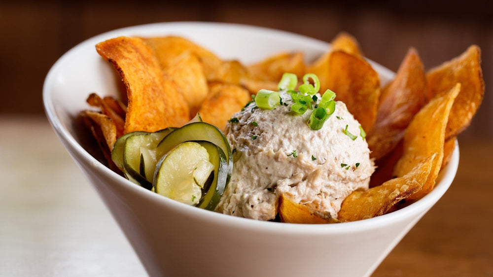 A bowl of smoked tuna dip with chips and pickles