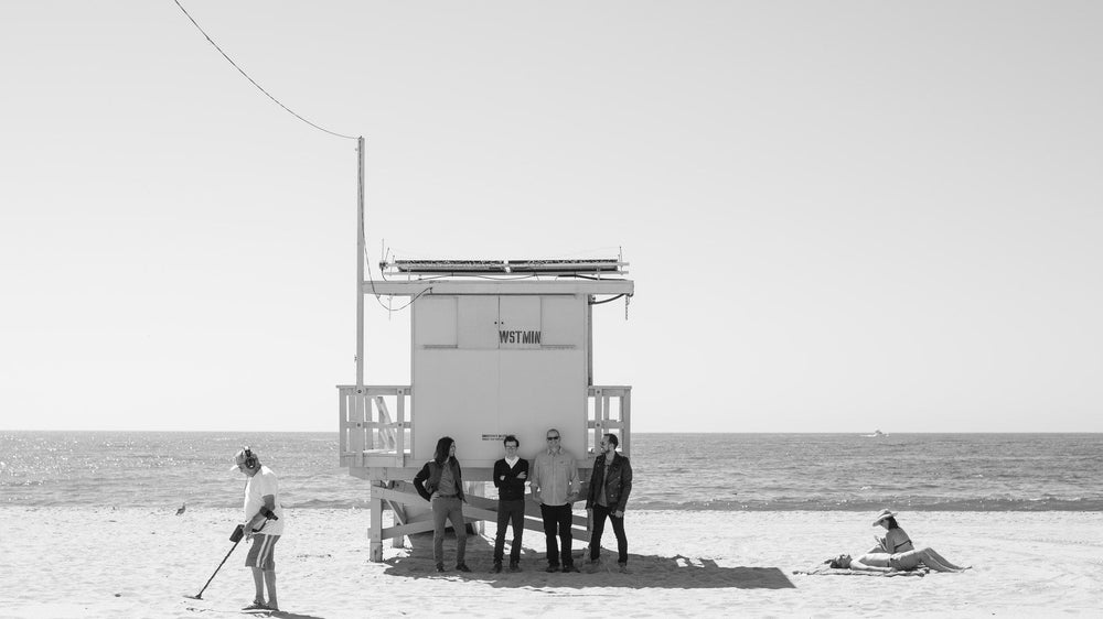 Black and white photograph of a group beside a lifeguard tower on an empty beach