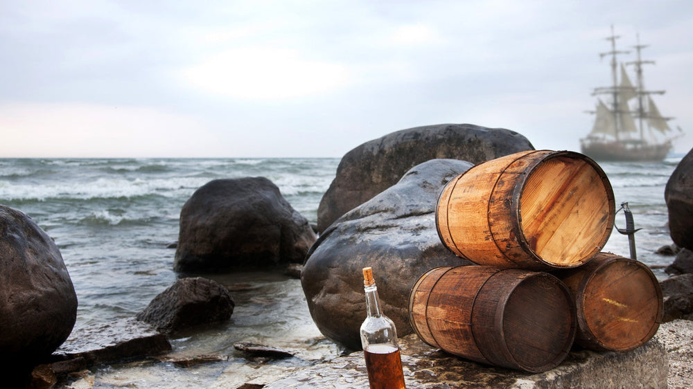 Rum barrels on the shore with a tall ship beyond